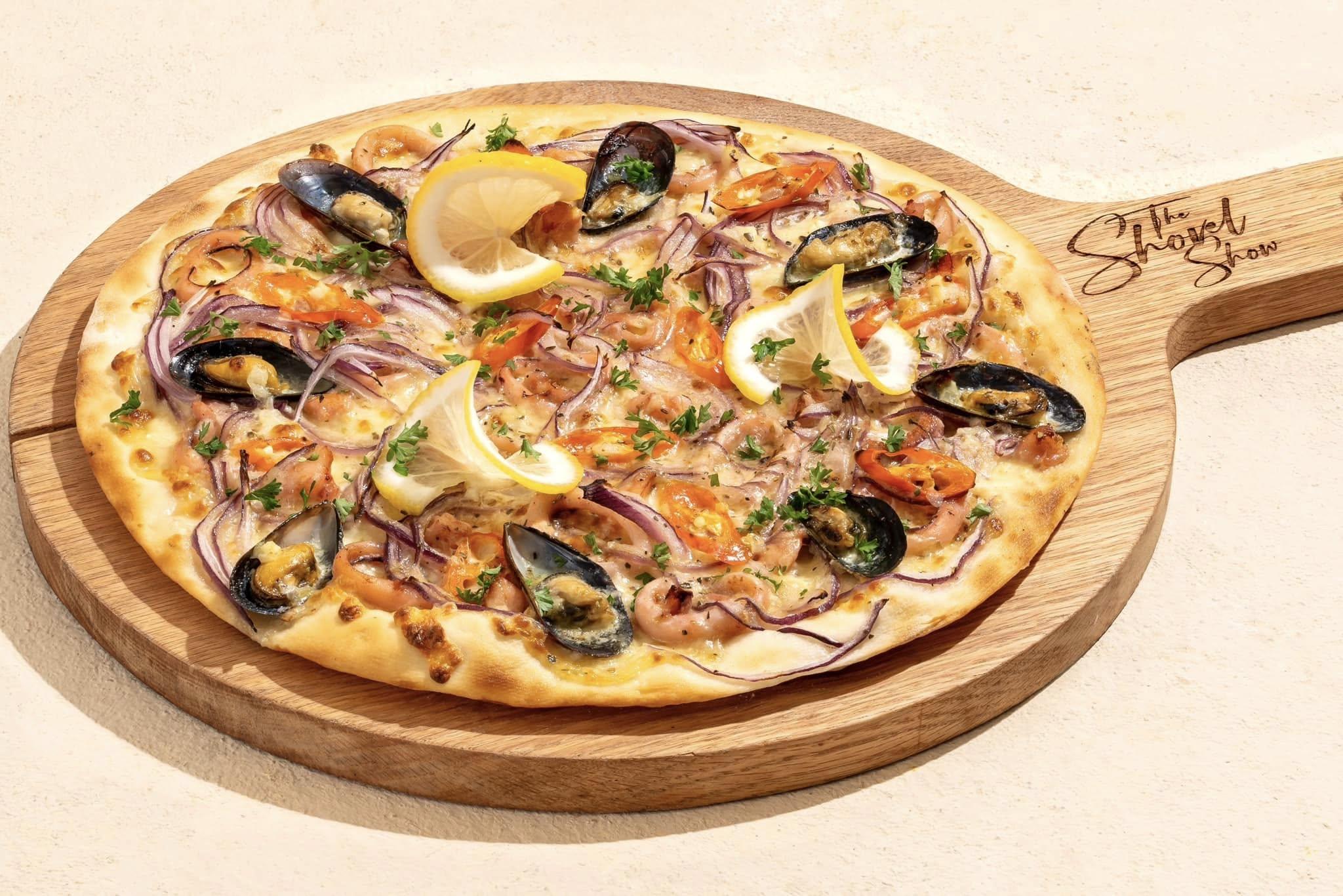 Paolo & Chi Pizzeria Old Quarter presents a seafood pizza featuring mussels, shrimp, and garnished with fresh parsley and lemon wedges 